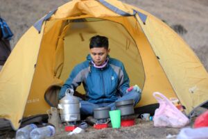 mężczyzna gotuje posiłek przed namiotem